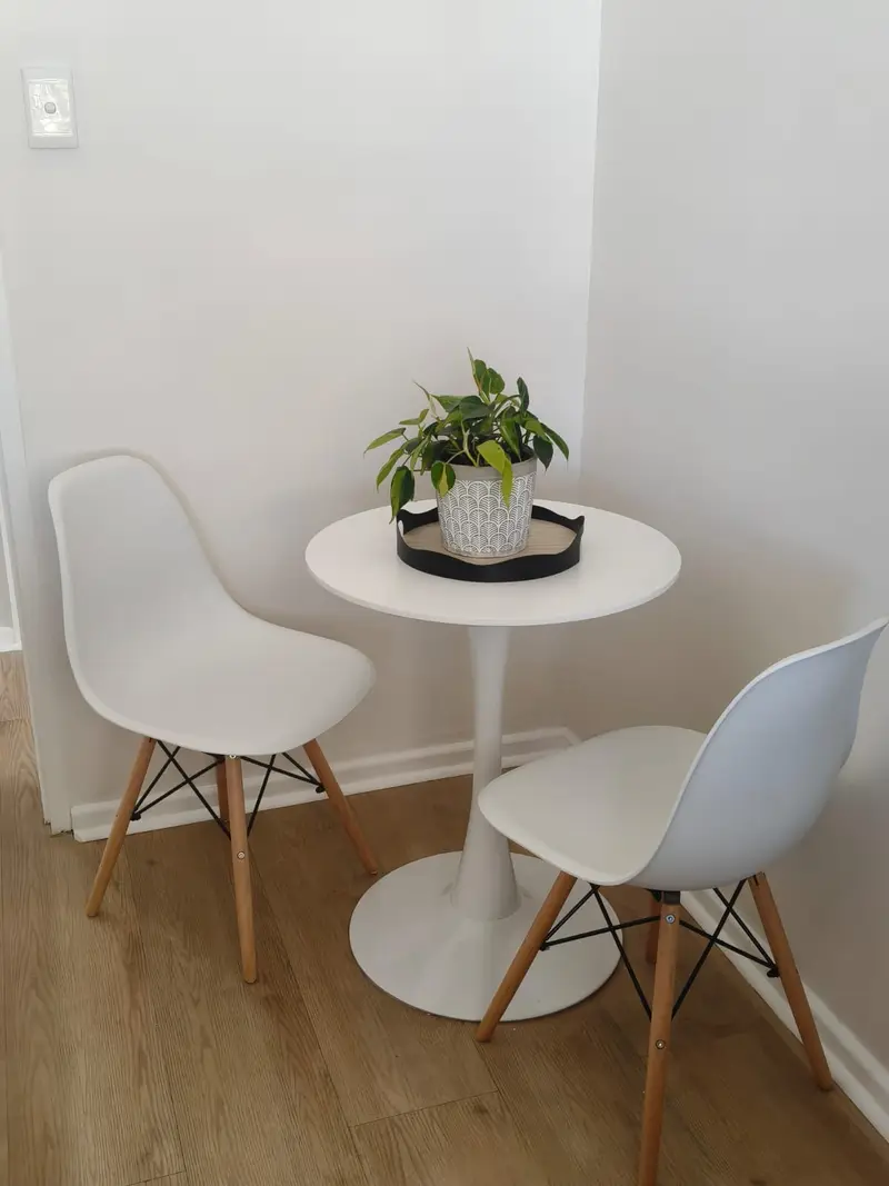 White bistro table with two chairs and a potted plant in a bright corner