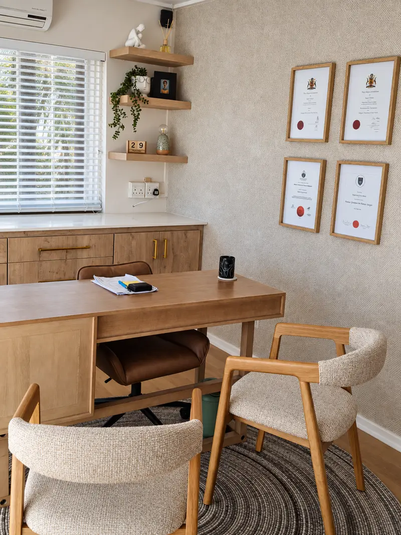 Consulting room with oak desk, bouclé chairs, floating shelves and framed qualifications on textured wallpaper